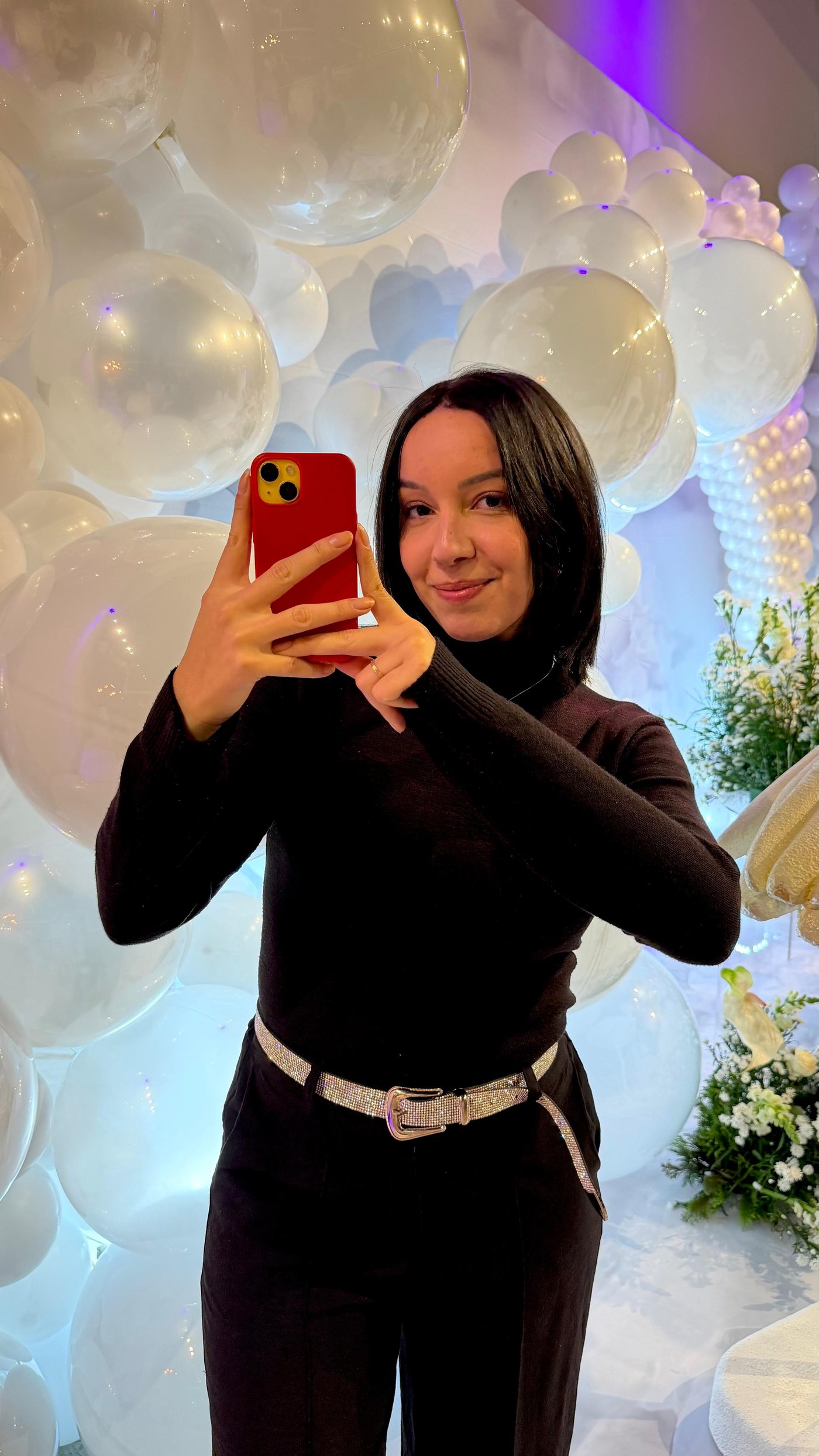 Ana Delphino, filmmaker, segurando o celular em frente a um arco de balões